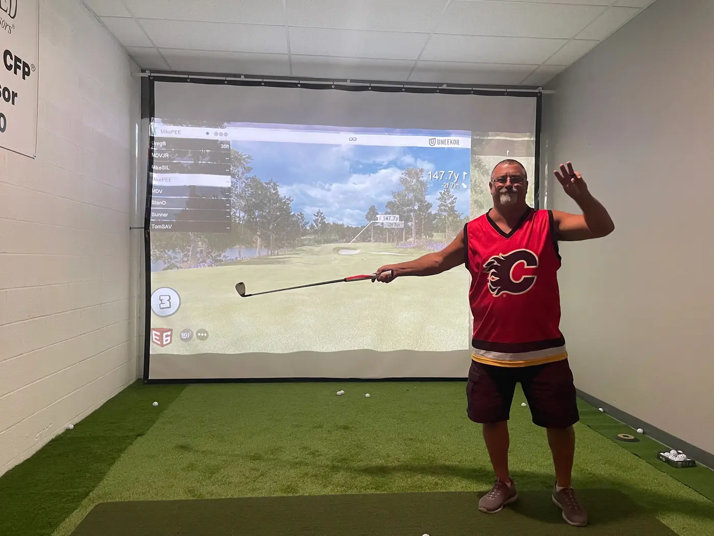 A golfer in a red jersey celebrating with his club raised in the simulator bay